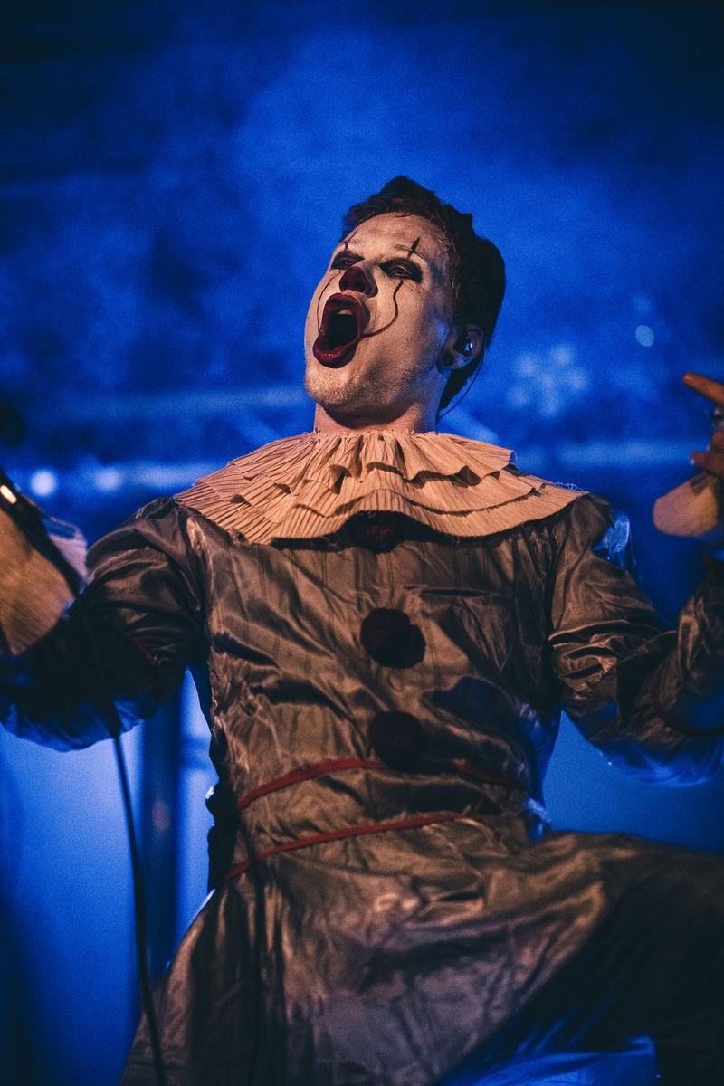 Geschminkte zanger van AnotherNow in clownspak schreeuwt, blauw licht