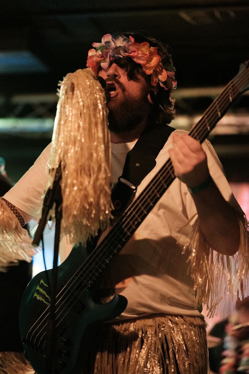 Bassist van Changing Tides in Hawaï-outfit met een rieten pruik