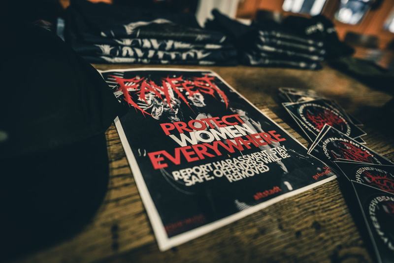 Poster op de merchtafel: Protect women everywhere. Report harassment. Stay safe.